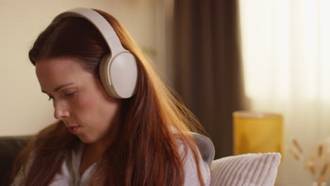 fotografía de cerca de una mujer con auriculares inalámbricos sentada en el sofá en casa escuchando música