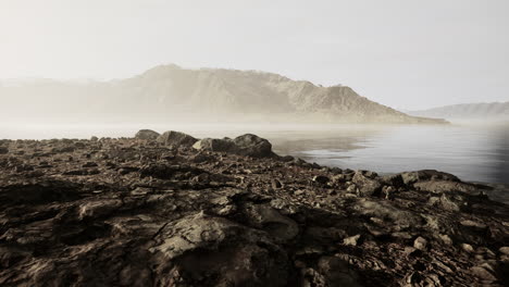 Clear-river-with-rocks-leads-towards-mountains-lit-by-sunset