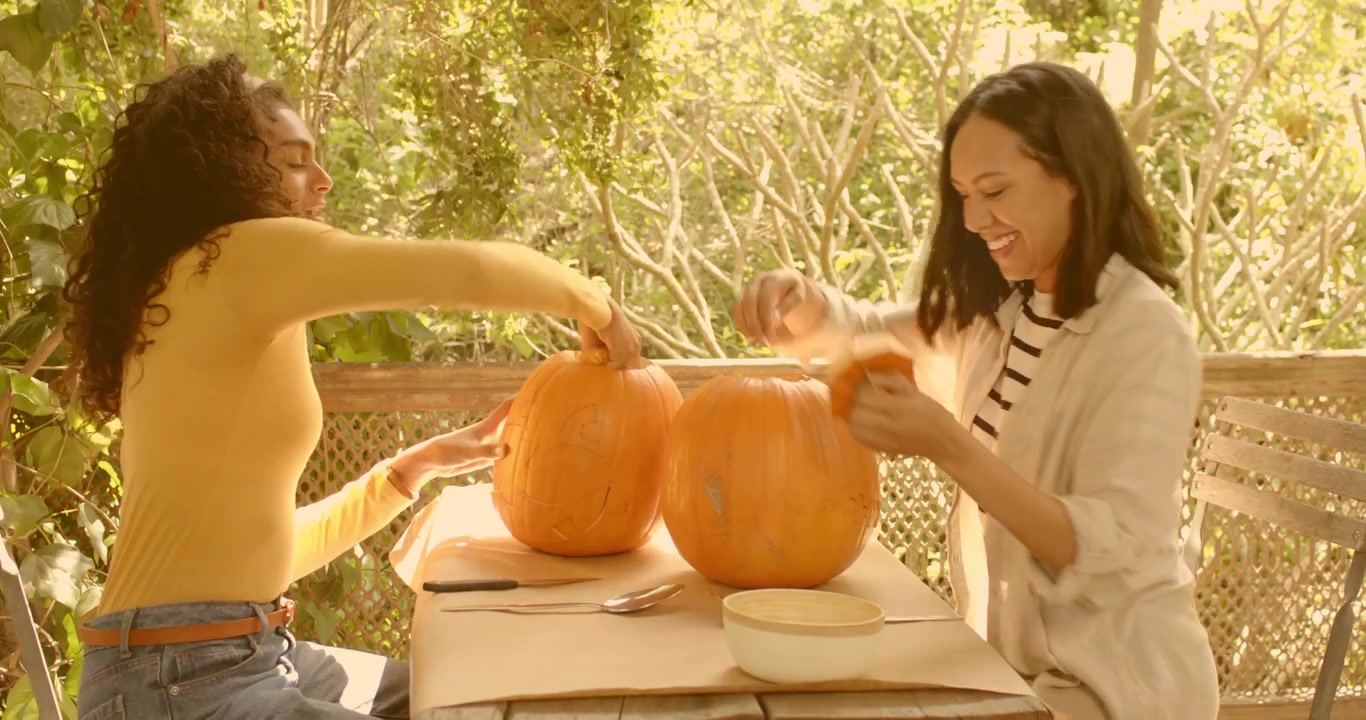 Friends placing pumpkins and carving lids at patio while digital icons floating for social sharing