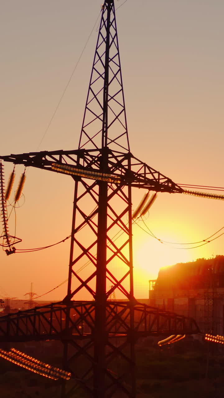 Industrial high voltage electricity tower. Silhouette of high voltage electric tower on sunset time. Industrial factory against the evening sky on sunset time background. Vertical video
