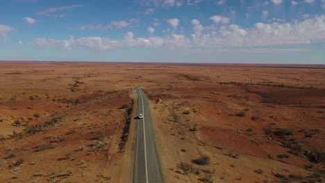 aerial: drone shot following a white 4x4 vehicle driving down an empty road in the australian outback near broken hill, australia