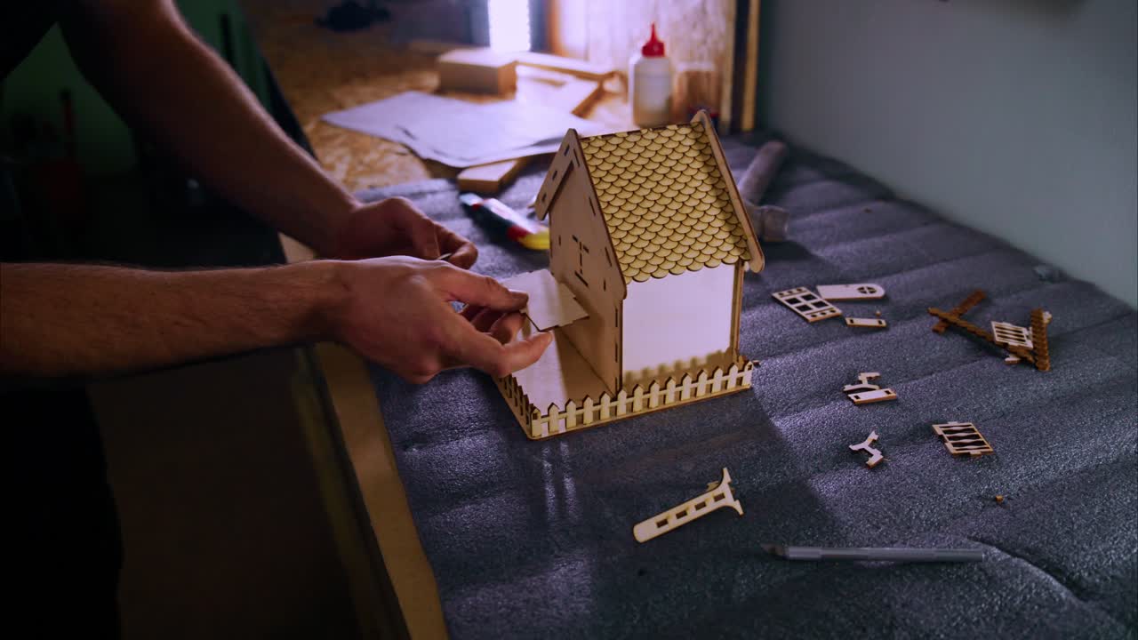 Mani che assemblano una casa modello in legno su un banco da lavoro