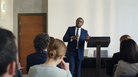 African-American-young-businessman-wearing-formal-clothes-speaking-at-the-conference-in-front-of-the-many-people