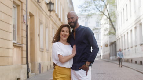 portrait of a happy interracial couple embracing and looking at camera in the old town street