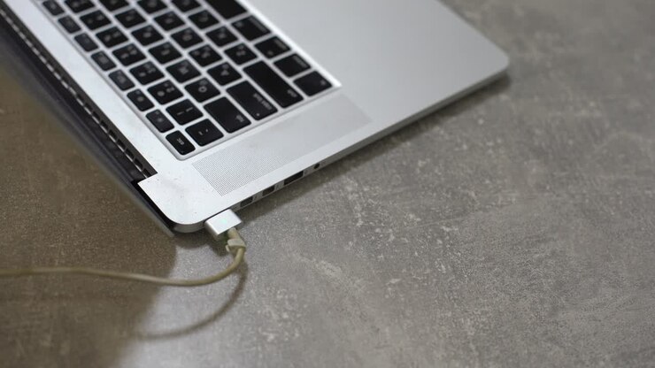 Mano che inserisce l'alimentatore nel laptop, tecnologia informatica quotidiana per uso personale
