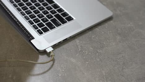 Hand-plugging-power-adapter-in-laptop,-everyday-computer-technology-personal-use