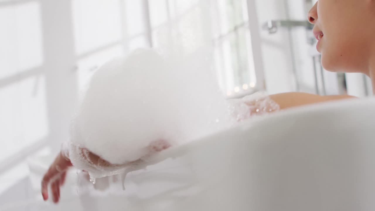 화장실에서 거품 욕조에 누워 있는 미소 짓는 두 인종의 여성의 비디오