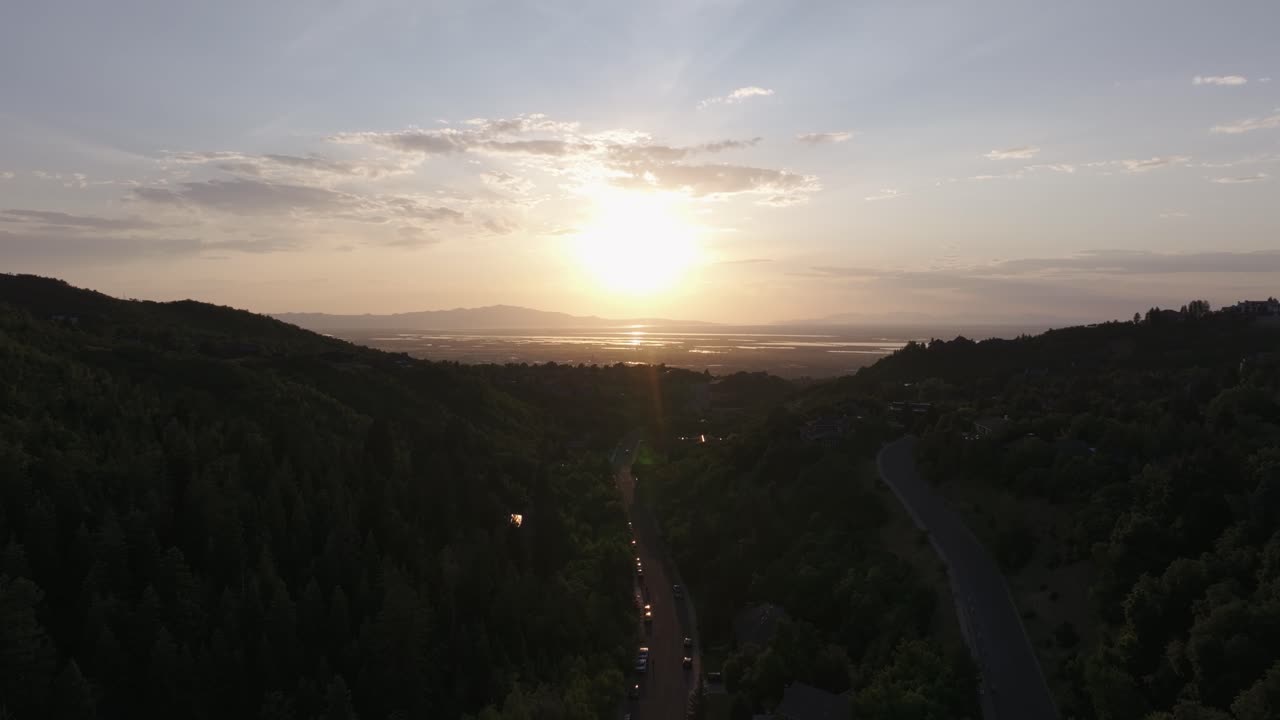Aerial drone shot from Bountiful Canyon in Utah at golden hour with road, forest, valley homes, Wasatch Mountains, cityscape, and the Great Salt Lake at sunset