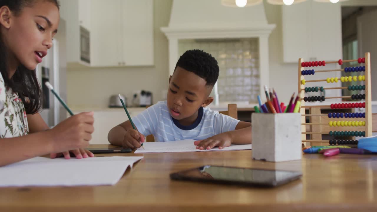 African american sister and brother sitting at kitchen table doing homework
