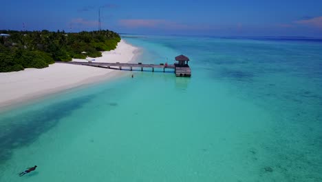 soft aerial drop towards stunning turquoise water where lone man floats in tranquillity