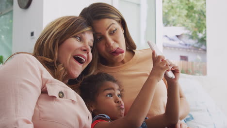familia hispana de varias generaciones en casa haciendo caras divertidas para tomarse una selfie en el teléfono móvil
