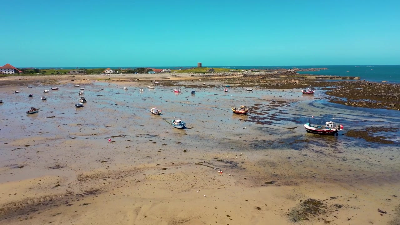 Riprese aeree con drone che rivelano pescherecci che si asciugano in un porto naturale sabbioso nel nord-ovest di Guernsey, con la Torre Martello sullo sfondo in una soleggiata giornata estiva
