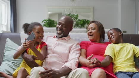 Happy-african-american-grandparents-and-grandchildren-sitting-on-sofa,-taking-selfie
