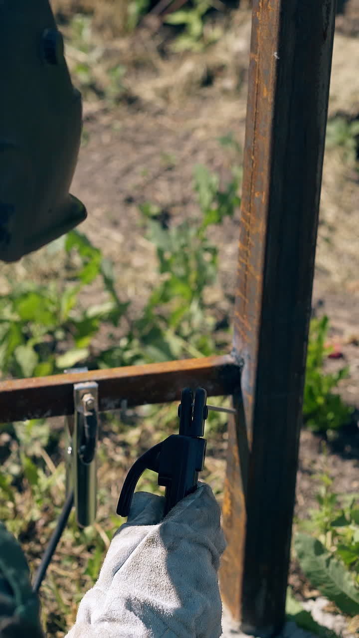 backside view worker in camouflage and mask welds and checks metal parts of country house fence in yard