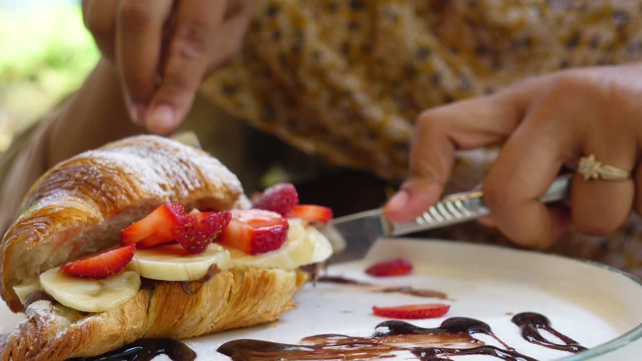 Mulher comendo um croissant com morangos e bananas