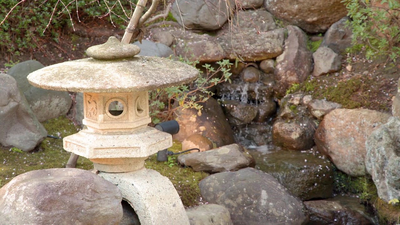 ภาพนิ่งของโคมไฟหินโทโร่ใกล้น้ำตกที่ไหลเชี่ยวในเมืองคานาซาวะ ประเทศญี่ปุ่น