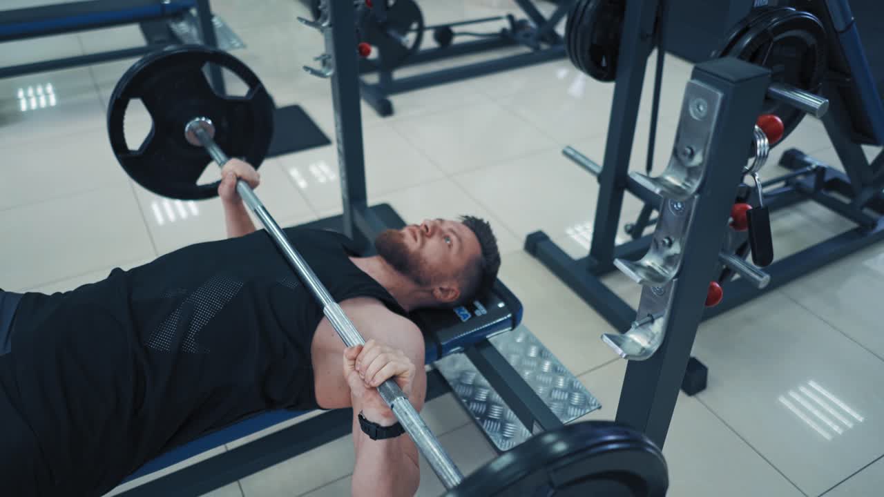 Strong bearded bodybuilder with barbell. Muscular man in black sportswear lifting up heavy barbell in gym. Close-up.