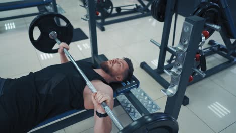 strong bearded bodybuilder with barbell. muscular man in black sportswear lifting up heavy barbell in gym. close-up.