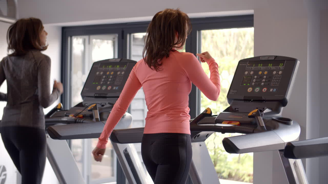 Two women exercise on running machines at a gym, back view