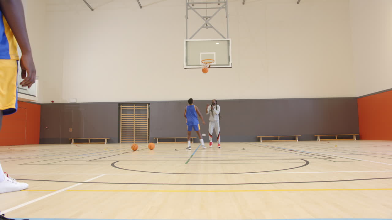Playing basketball in gym, coach training player on shooting techniques