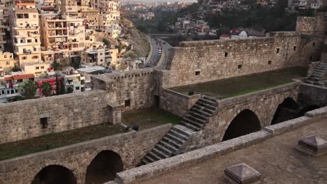 Vista-épica-Del-Pueblo-En-Una-Colina-Y-Un-Valle-Que-Conduce-Hacia-Las-Montañas-Sobre-Las-Ruinas-Del-Antiguo-Castillo-De-Piedra-En-Trípoli,-Norte-Del-Líbano