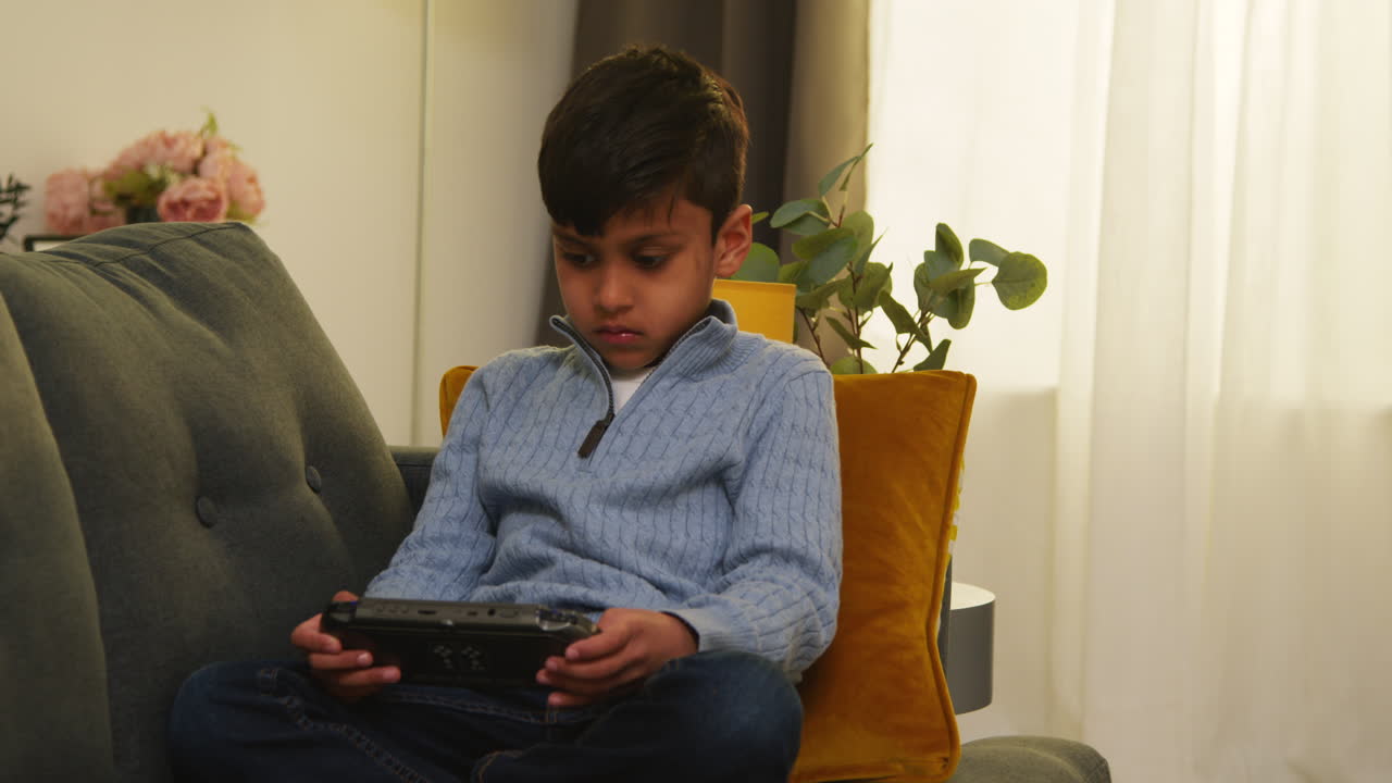 niño sentado en el sofá en casa jugando a un juego o transmitiendo a un dispositivo de juego portátil
