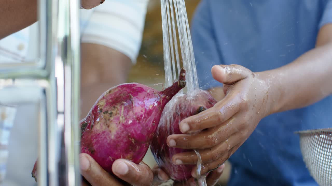 Faucet is running as two hands are rinsing purple yams at kitchen sink for cooking