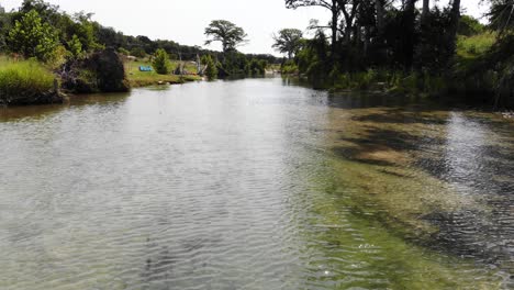 hovering for a moment and then quickly flying just above the river in an open section towards a wooded section - aerial footage of the blanco river in wimberly, tx