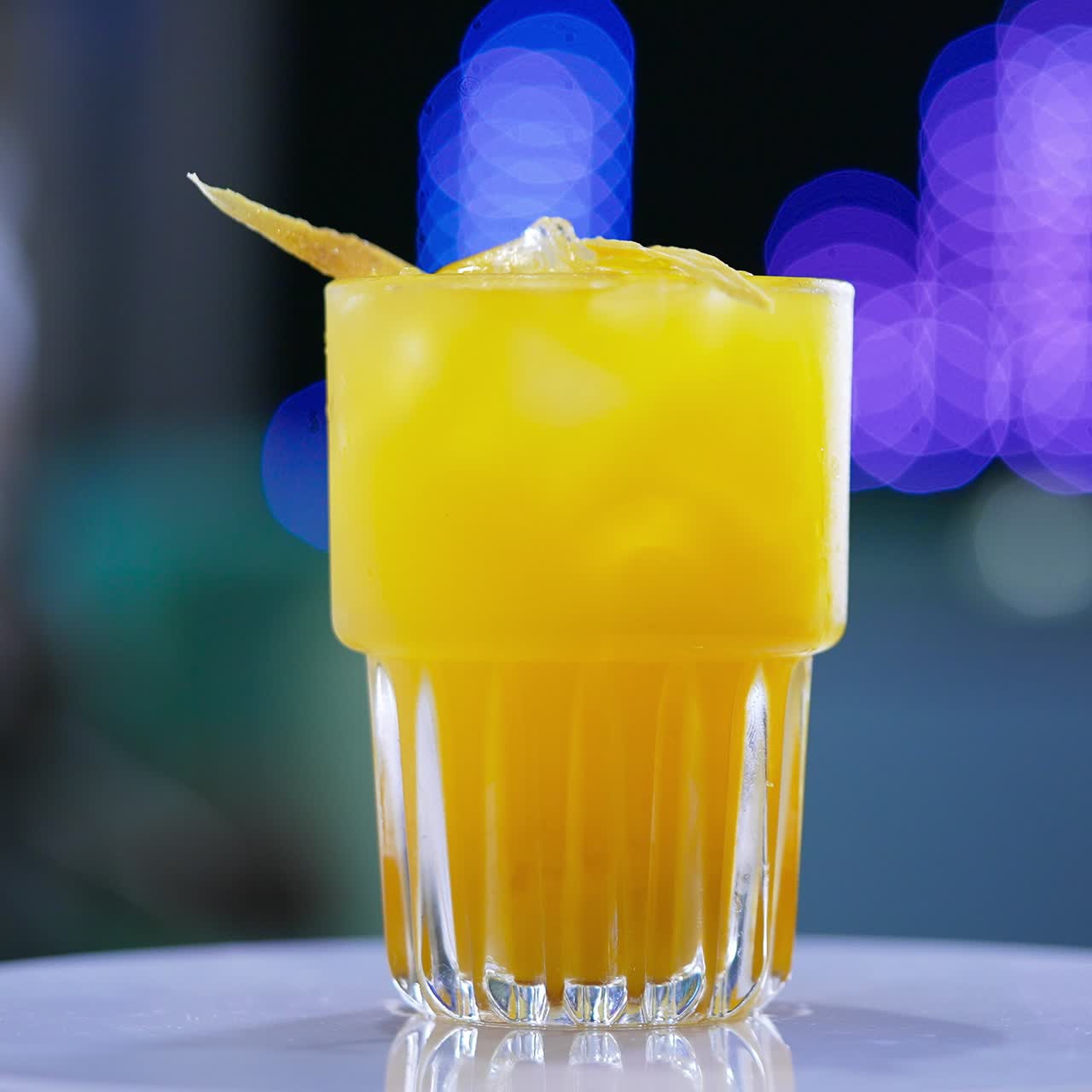 A glass filled to the top with beverage of yellow color. Savory cocktail on the rotating table close up. Blurred backdrop