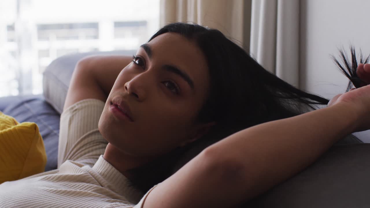 acercamiento de género fluido masculino jugando con el cabello mientras está acostado en el sofá en casa