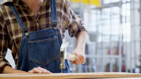 female welder hammering nail on a wooden plank 4k