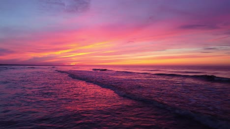 aerial dolly out revealing the softness of the waves passing over the sea in an epic and incredible pink and yellow sunset