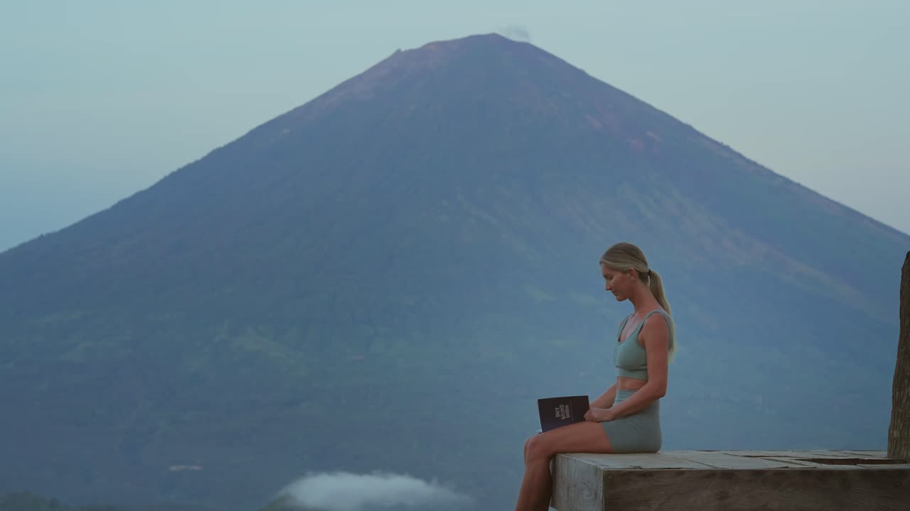 Woman takes deep breath and continues working on personal development with journal, Mount Agung in background