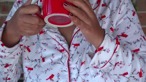 medium shot of black woman drinking warm coffee while wearing warm pajamas