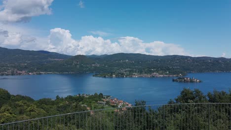 Aerial-shot-of-an-infinity-pool-overlooking-a-lake-with-green-meadows-and-some-picturesque-buildings,-in-Pella,-Piedmont-in-Italy