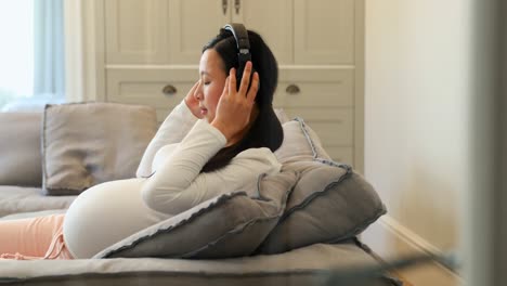 pregnant woman listening to music on headphones in living room 4k