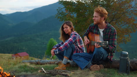 positive couple date outdoors in mountains. two lovers play guitar by campfire.