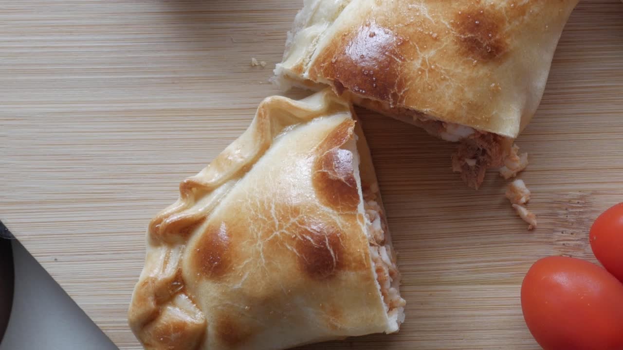 Close-up of golden empanadillas with crimped edges on a wooden board, warm and inviting