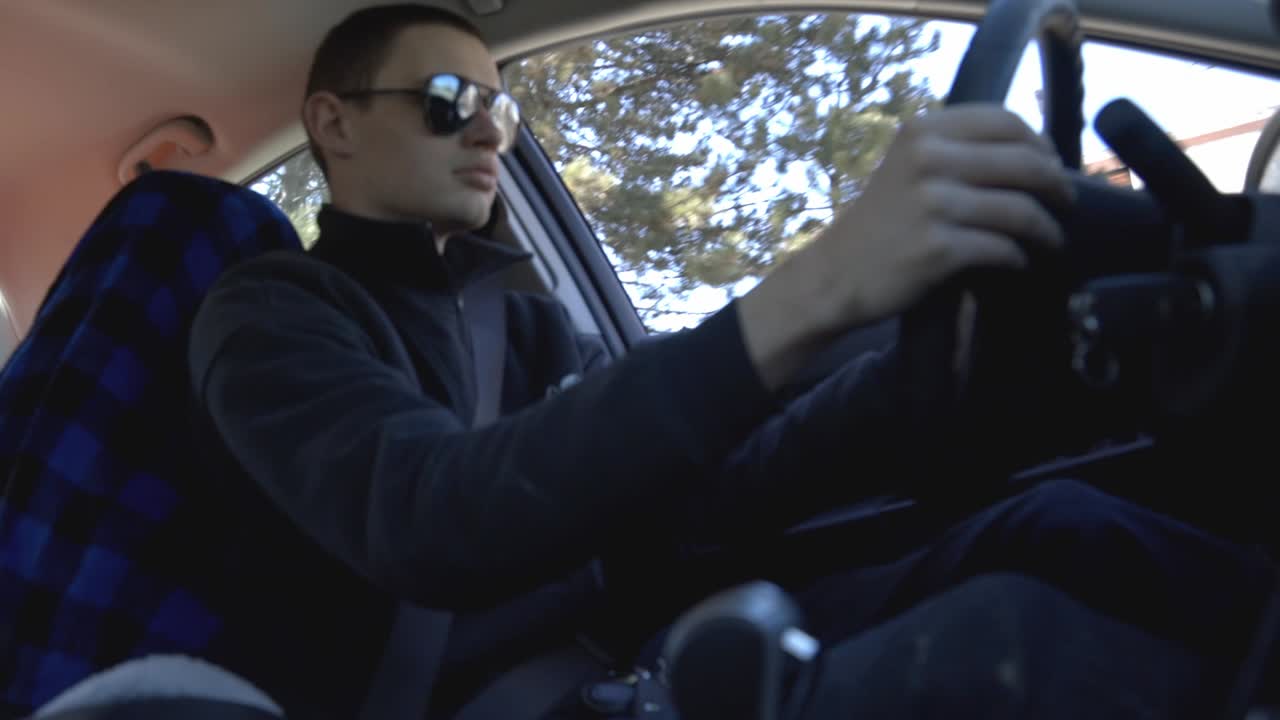 A Young Man Wearing Shades And Black Jacket Driving His Car - Low Angle Shot