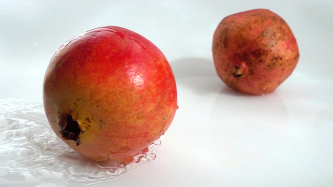 Frugten er granatæbler i vand på en hvid baggrund. Slowmotion.