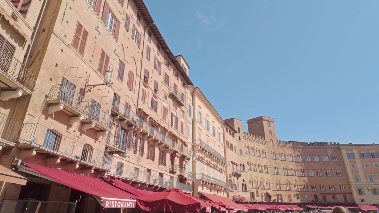 Veduta di Piazza del Campo a Siena che mostra le facciate medievali curve, con un accenno delle tende rosse in basso che incorniciano la forma della piazza.