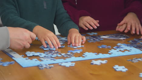 close up de la familia sentada alrededor de la mesa en casa haciendo rompecabezas juntos