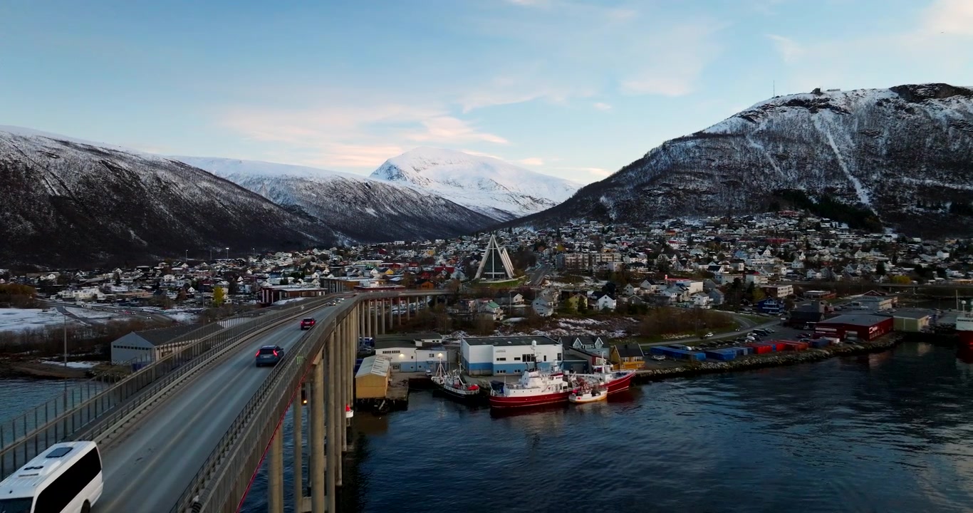 Mouvement de recul du drone près du pont de la ville de Tromso avec de la circulation et une vue sur un paysage urbain enneigé.