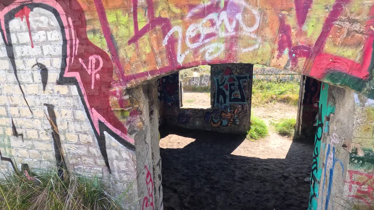 Camera glides through graffiti-covered entrance into sunlit, abandoned stone fort with vibrant murals