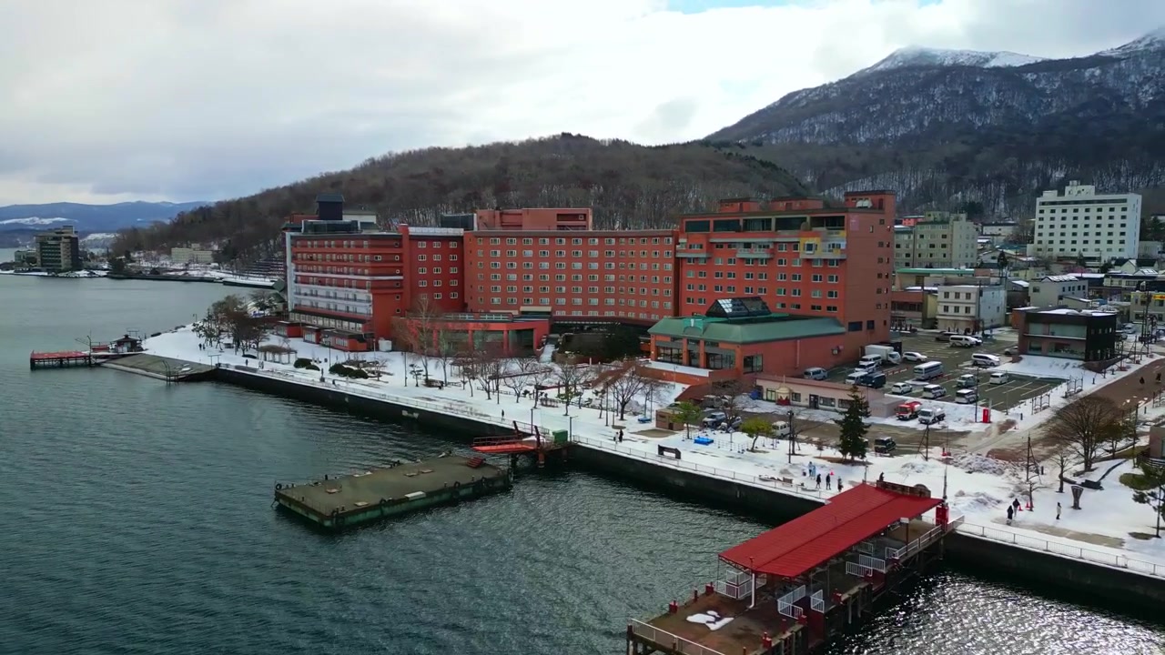 Omfattende luftfoto av store hoteller ved innsjøen, brygger og det snødekte landskapet i byen Toyako omgitt av fjell i Hokkaido, Japan