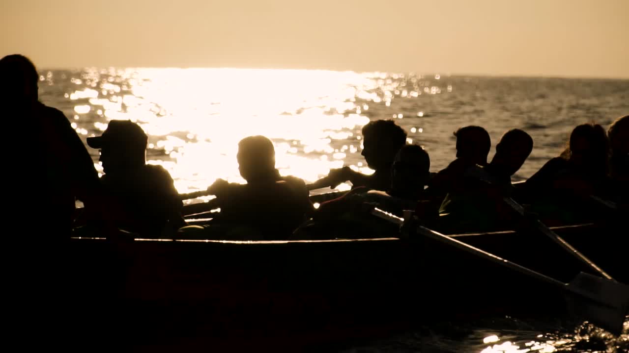 밝은 일몰이나 일출 앞에서 바다에서 노를 젓는 사람들의 실루엣
