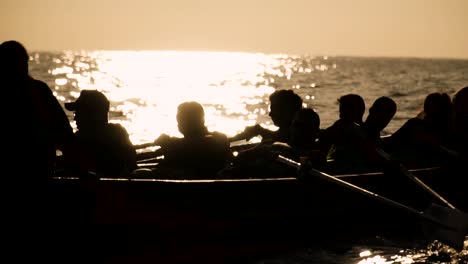 silueta de un equipo de personas remando en el mar frente a un brillante atardecer o amanecer