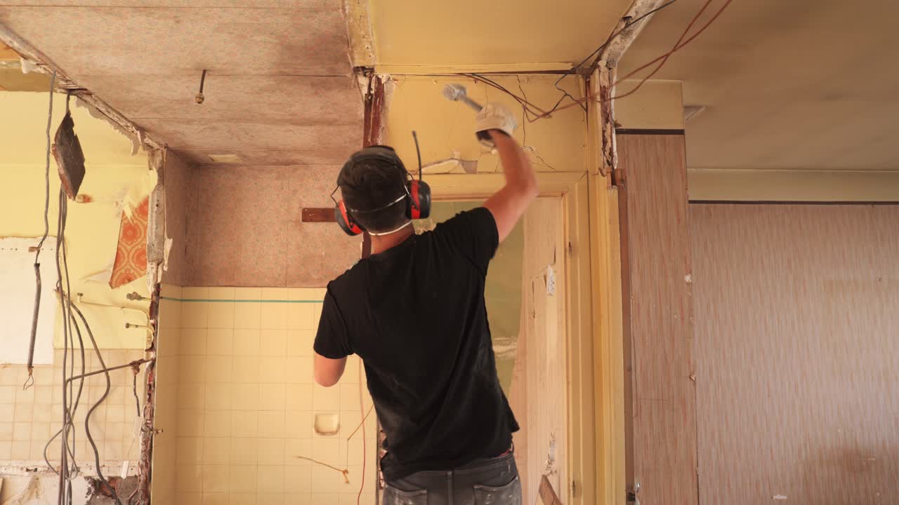 Pria merobohkan dinding dan kusen pintu di dalam apartemen yang sedang dibongkar dengan palu godam, bidikan lebar statis