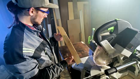 concentrated young bearded joiner in goggles and a cap checks the work piece