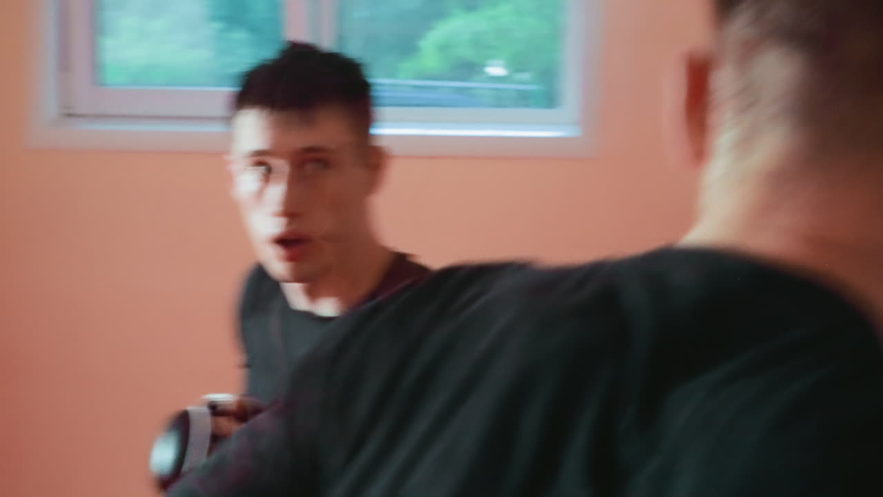 Pugilist in black shirt wearing gloves maintains guard position during combat training inside gym with focus and determination, showing intensity, concentration, strength, and readiness for boxing match